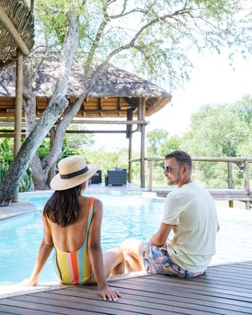 couple men and women on safari in South Africa relaxing by the pool of a luxury safari lodge , Asian women and European men on safari in South Africa