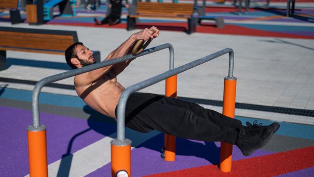 Shirtless man doing horizontal balance on parallel bars at sports ground