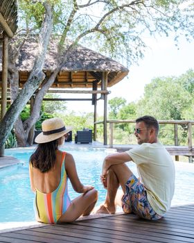 couple men and women on safari in South Africa relaxing by the pool of a luxury safari lodge , Asian women and European men on safari in South Africa