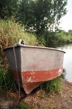 A motor boat is parked at the shore of a lake or river in the evening at sunset or early in the morning. The boat is in a quiet place next to the reeds and is ready for fishing.