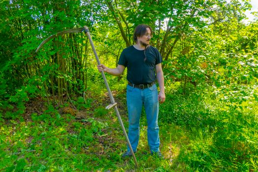 A man mows the grass with a hand scythe. Mow the grass with an old scythe. The farmer traditionally mows the lawn. The mower mows the green grass with a manual metal scythe.