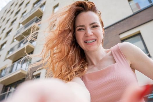 Beautiful young red-haired woman with braces on her teeth smiling in the summer outdoors.