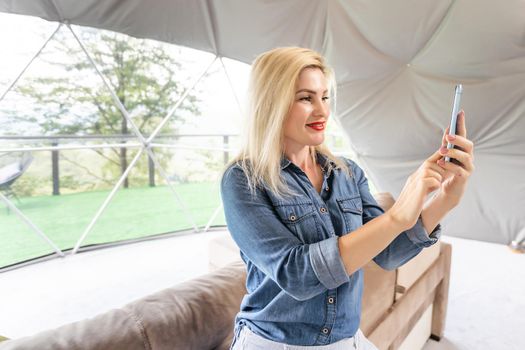 Image of happy nice woman smiling and using cellphone at living room.