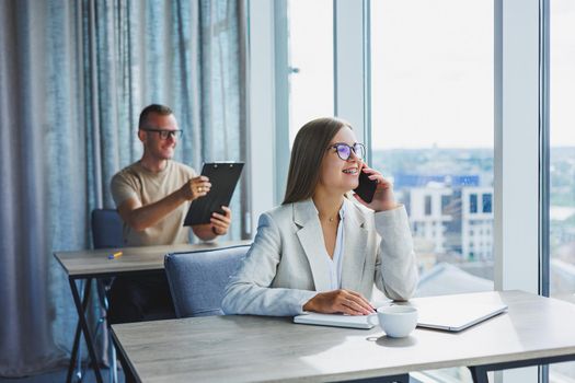 Portrait of a female manager in formal attire doing office work and talking on the phone, a successful european female boss in optical glasses for vision correction, posing at her desk