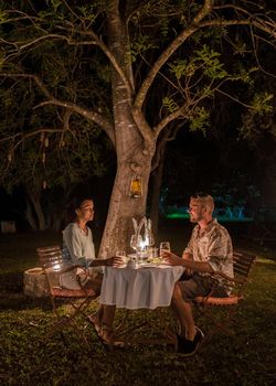 couple on safari in South Africa, Asian women and European men having a bush dinner with candlelight at night. Romantic dinner at night in the bush during a luxury safari in South Africa