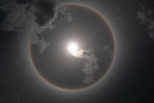 The beauty of the sun with a circular rainbow surrounded by bright skies and white clouds. Phenomenon, sun halo.
