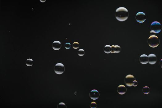 Flying soap bubbles on black background. Abstract soap bubbles with colorful reflections. Soap bubbles in motion background.