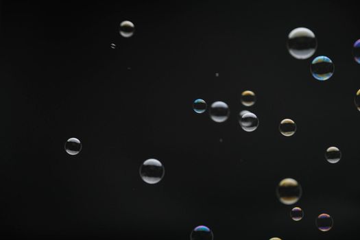 Flying soap bubbles on black background. Abstract soap bubbles with colorful reflections. Soap bubbles in motion background.