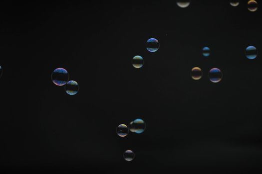 Flying soap bubbles on black background. Abstract soap bubbles with colorful reflections. Soap bubbles in motion background.