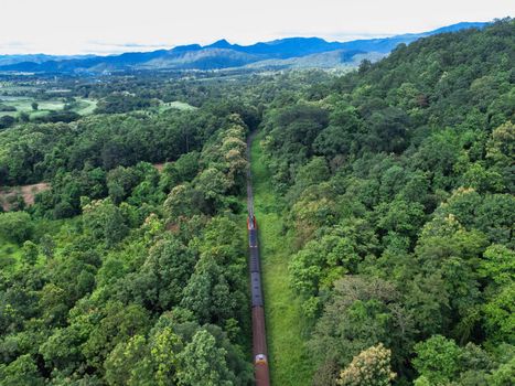 Aerial view of a drone on a railway track in a rural landscape with green forest during the rainy season. The drone flew above the forest and saw the railroad tracks in the distance.