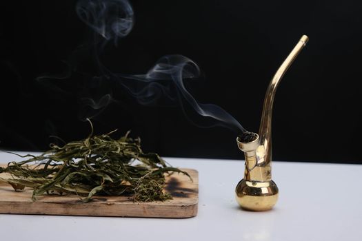 Close-up of cannabis leaves on a wooden board and smoke coming out of a pipe on a black background. Cannabis legalisation.