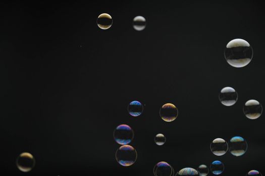 Flying soap bubbles on black background. Abstract soap bubbles with colorful reflections. Soap bubbles in motion background.