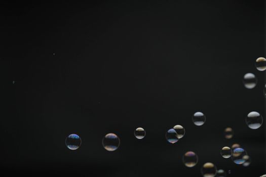 Flying soap bubbles on black background. Abstract soap bubbles with colorful reflections. Soap bubbles in motion background.