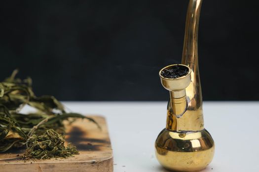 Close-up of cannabis leaves on a wooden board and smoke coming out of a pipe on a black background. Cannabis legalisation.