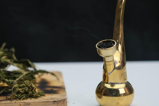 Close-up of cannabis leaves on a wooden board and smoke coming out of a pipe on a black background. Cannabis legalisation.