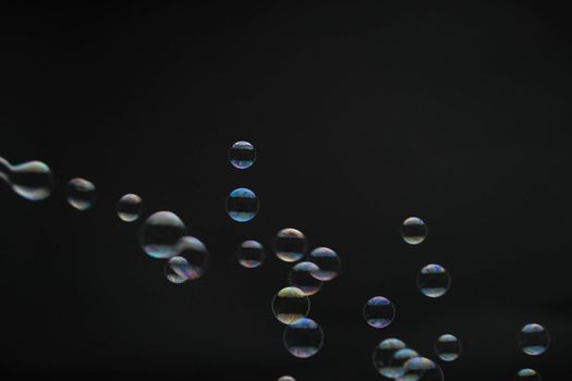 Flying soap bubbles on black background. Abstract soap bubbles with colorful reflections. Soap bubbles in motion background.