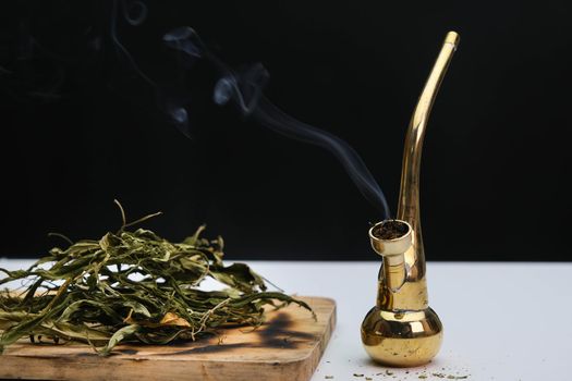 Close-up of cannabis leaves on a wooden board and smoke coming out of a pipe on a black background. Cannabis legalisation.