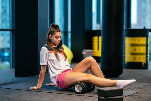 Young woman using a foam roller while doing stretching exercises in the gym.