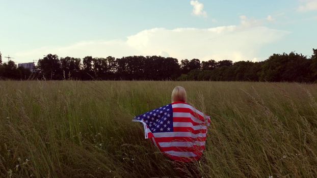 Young happy woman waving USA stars and stripes flag in golden sunset sunshine field.