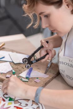 Workplace of the mosaic master: women's hands holding tool for mosaic details in the process of making a mosaic. Close-up. Creative process. Masterclass handmade