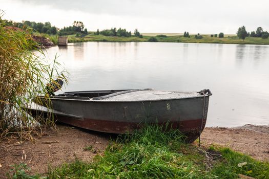 A motor boat is parked at the shore of a lake or river in the evening at sunset or early in the morning. The boat is in a quiet place next to the reeds and is ready for fishing.