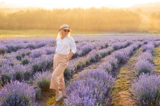 Young blond woman traveller wearing straw hat in lavender field surrounded with lavender flowers