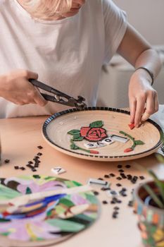 Workplace of a mosaic master: female hands laying out a mosaic element on the table. Master lays the mosaic on a plate Masterclass handmade