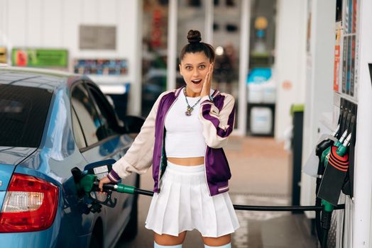 Cheerful young woman brunette filling her car with fuel at a gas station