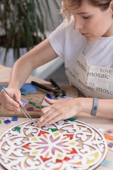 Workplace of the mosaic master: women's hands holding tool for mosaic details in the process of making a mosaic. Close-up. Creative process.