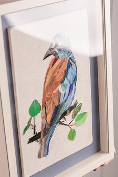 Mosaic bird. Handmade decoration. Frame decoration. The frame stands on the table near the wall