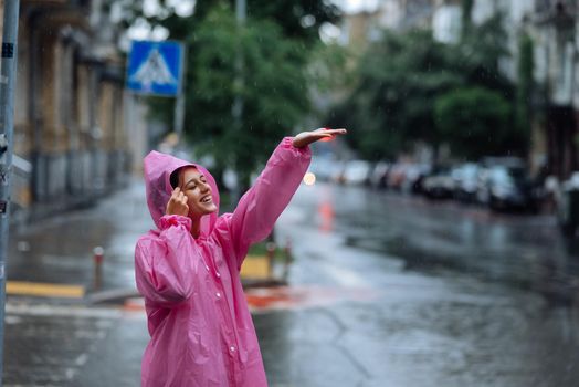 Young smiling woman with a pink raincoat on the street while enjoying a walk through the city on a rainy day.
