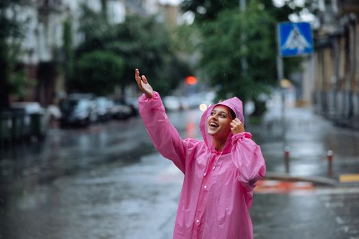 Young smiling woman with a pink raincoat on the street while enjoying a walk through the city on a rainy day.