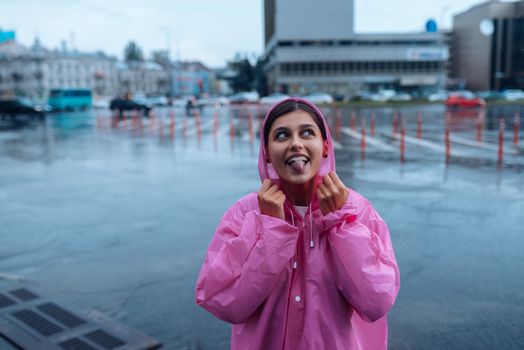 Young smiling woman with a pink raincoat on the street while enjoying a walk through the city on a rainy day.