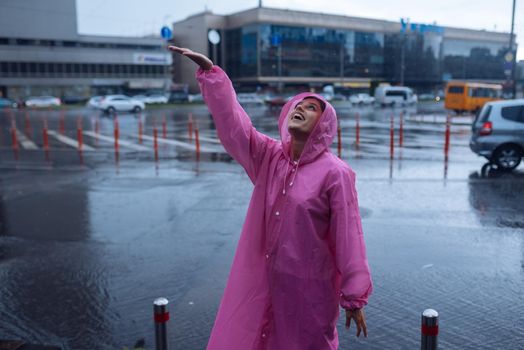 Young smiling woman with a pink raincoat on the street while enjoying a walk through the city on a rainy day.