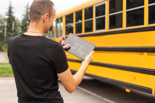 male Teacher Or Student With Digital Tablet near the school bus. video chat.