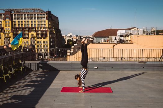 Beautiful young woman working out outdoors and doing yoga handstand exercise on yoga mat