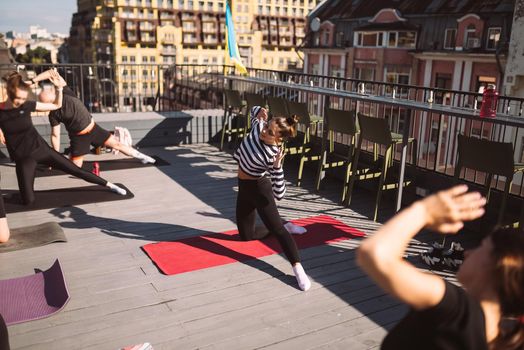 Yogi woman and diverse group of young sporty people practicing yoga, female students training at house's roof. Well being, wellness concept