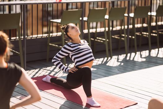 Yogi woman and diverse group of young sporty people practicing yoga, female students training at house's roof. Well being, wellness concept