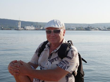 portrait of a smiling middle-aged man in sunglasses with a backpack on the sea.
