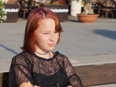 portrait of a teenage red-haired girl squinting from the sun.