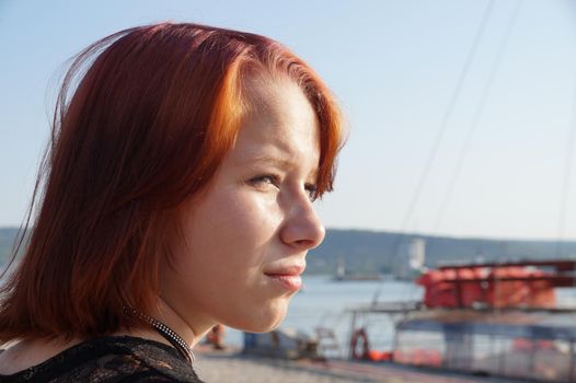 portrait of a teenage red-haired girl squinting from the sun, copy space