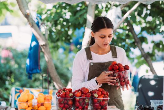 Young positive salesgirl at job, selling sells home-grown vegetables and fruits in vegetable shop