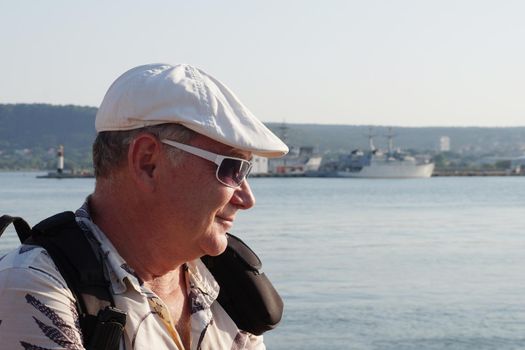 portrait of a smiling middle-aged man in sunglasses with a backpack on the sea, side view