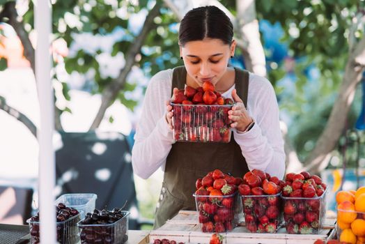 Young positive salesgirl at job, selling sells home-grown vegetables and fruits in vegetable shop