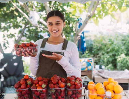 Young positive salesgirl at job, selling sells home-grown vegetables and fruits in vegetable shop