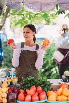 Young positive salesgirl at job, selling sells home-grown vegetables and fruits in vegetable shop