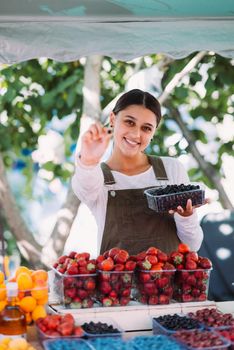 Young positive salesgirl at job, selling sells home-grown vegetables and fruits in vegetable shop