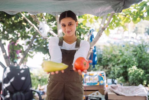 Young positive salesgirl at job, selling sells home-grown vegetables and fruits in vegetable shop