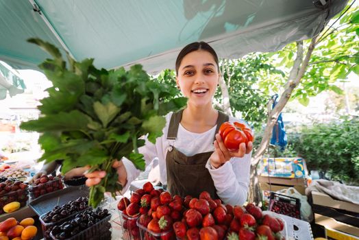 Young positive salesgirl at job, selling sells home-grown vegetables and fruits in vegetable shop