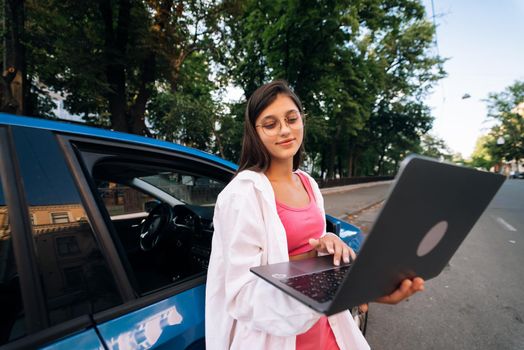 A young woman uses a laptop near a car in city center outdoors